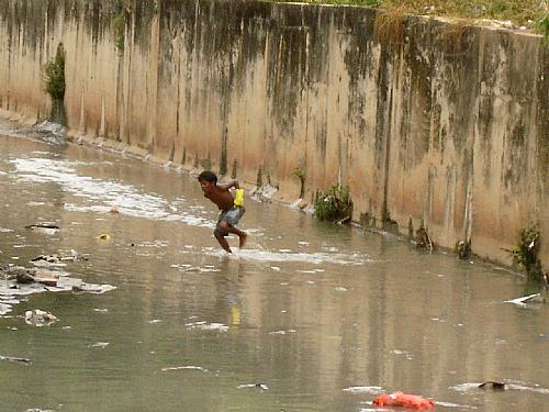 Menino se diverte nas águas da chuva; perigo de doença